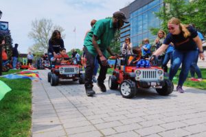 Parents and caregivers guide children with special needs in their modified cars down the sidewalk