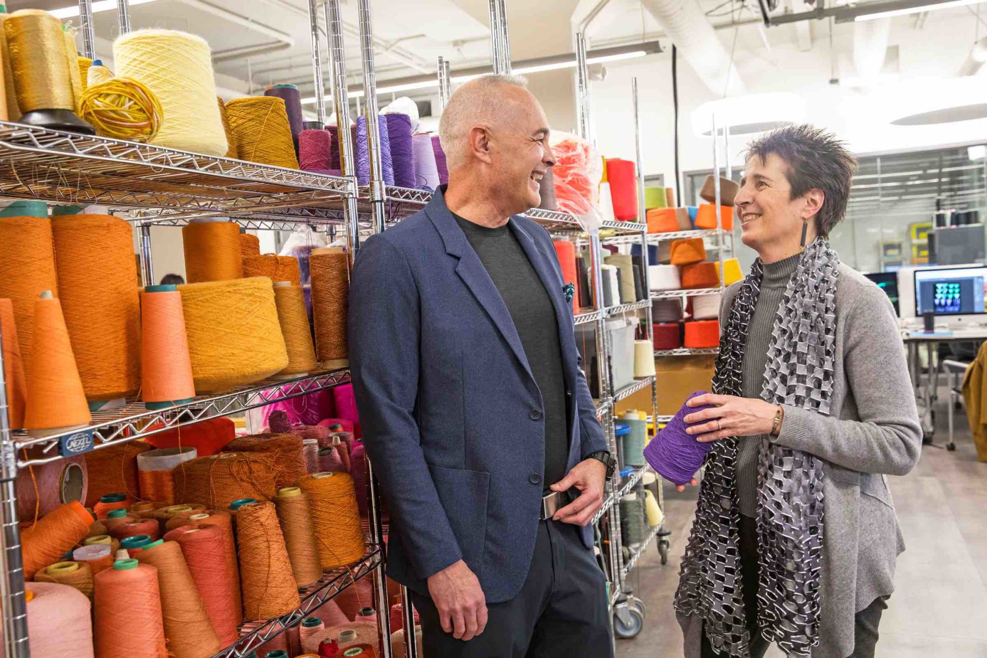 Two faculty members stand by spools of yarn