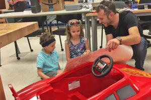 A student works with two children by a red toy car