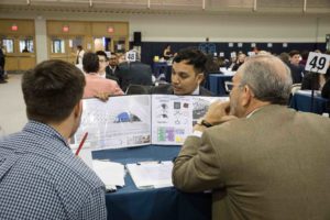 A student shows off his portfolio to two employers at a job fair