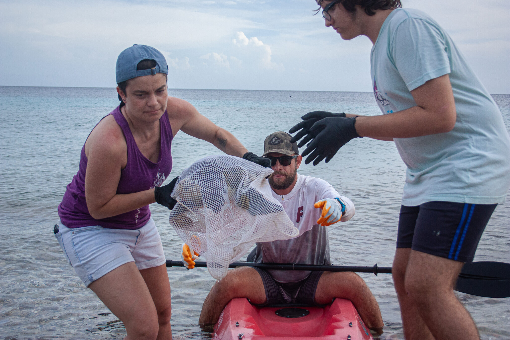Three people lifting a sea turtle out of a kayak on the shore of the ocean